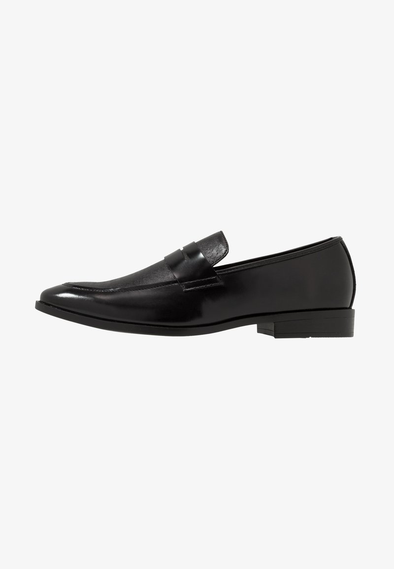 Mocassin homme en cuir noir avec un petit talon, un bout arrondi et un détail de bride sur le dessus, vu de profil sur fond blanc.