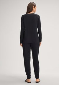 Zwart loungewear-set met een lang mouwtop met kantaccenten en loszittende broek met gathered hems, gemaakt van zachte stof.