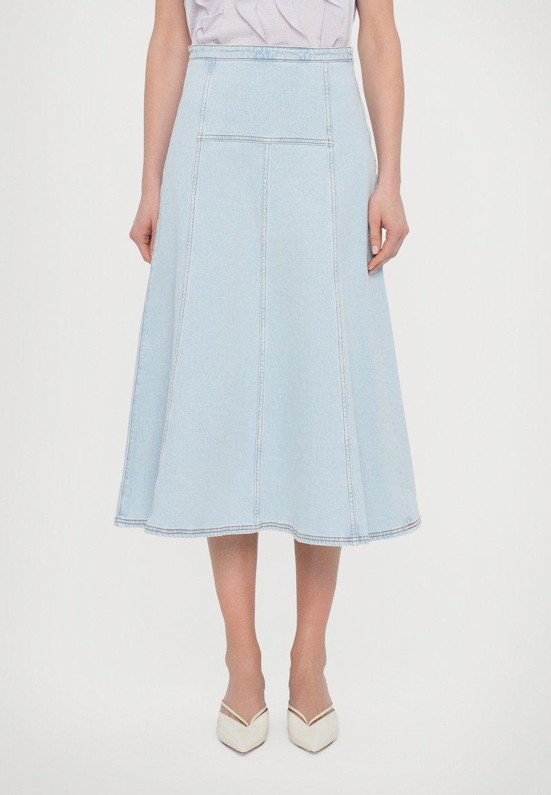 Light blue denim midi skirt with a flared shape, visible stitching, and two back pockets. Completed with white pointed shoes.