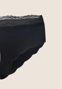 Czarne damskie majtki z falbaniastymi brzegami i koronkowym pasem w tle o jasnobeżowym kolorze.