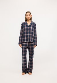Námornícky károvaný pyžamový set, ktorý obsahuje voľný tričko s gombíkmi a golierom a zodpovedajúce nohavice. Tartan vzor s červenými a bielymi pruhmi.