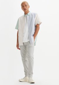Short-sleeve, button-up shirt in light colors with striped patterns, paired with light gray pants and white sneakers. Slim fit design.