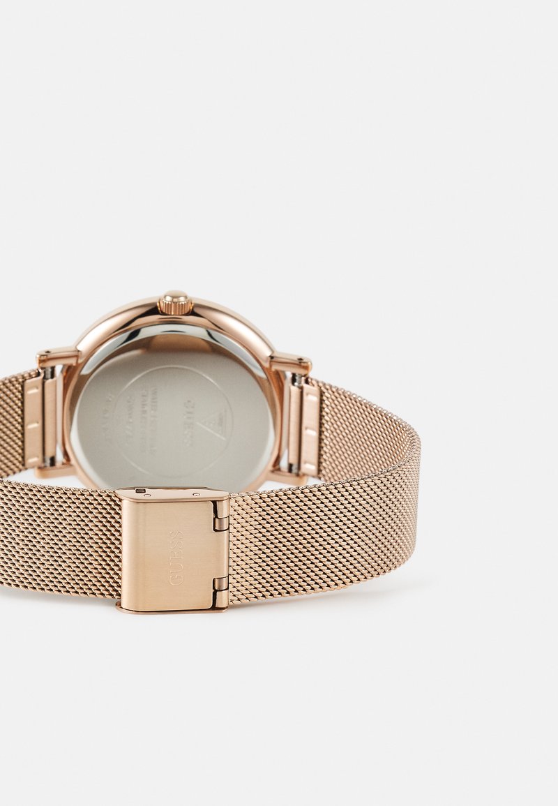 Montre en or rose avec un bracelet en maille et un boîtier rond. L'arrière présente une surface argentée poli. Le fermoir comporte un logo gravé.