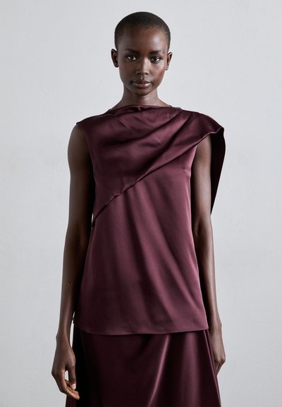 Burgunderfarbene ärmellose Bluse mit drapiertem Design, aus glattem Material gefertigt und mit asymmetrischem Saum, ergänzt durch eine figurbetonte Silhouette.