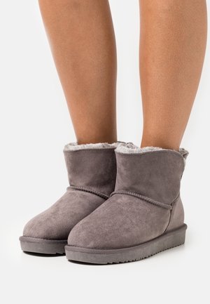 Grey suede ankle boots with faux fur lining, rounded toe, and a flat rubber sole, featuring seamless stitching around the upper.