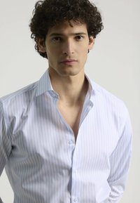 Camisa blanca de vestir con rayas verticales azul claro, hecha de una tela suave. Cuenta con un cuello extendido y una parte delantera con botones.
