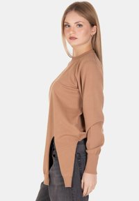 Maglione marrone lavorato a maglia con maniche lunghe, scollatura rotonda e spacchi laterali. Abbinato a jeans scuri, ha una texture morbida e un fit casual.