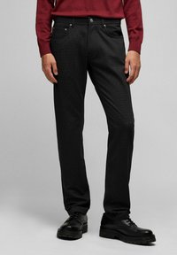 Pantalon noir texturé à coupe droite, avec cinq poches et des accessoires en métal, associé à des chaussures solides noires.
