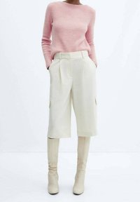 Pull en tricot rose clair avec un col bateau, associé à un short cargo crème taille haute et des bottes beiges à talons montantes.