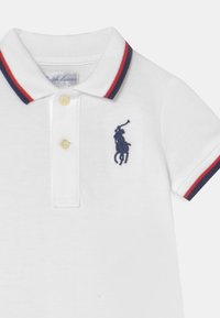 Bílá polokošile s texturovanou tkaninou, s límcem v červených a modrých pruzích, s dvou knoflíkovou légou a námořnickou vyšitou logem na hrudi.