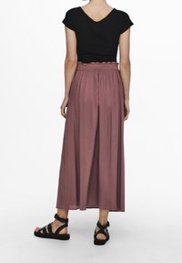 Schwarzes Oberteil mit kurzen Ärmeln, rosa Maxirock mit einem rüschierten Bund und schwarze Sandalen mit Riemchen. Glatter Stoff und lässige Passform.