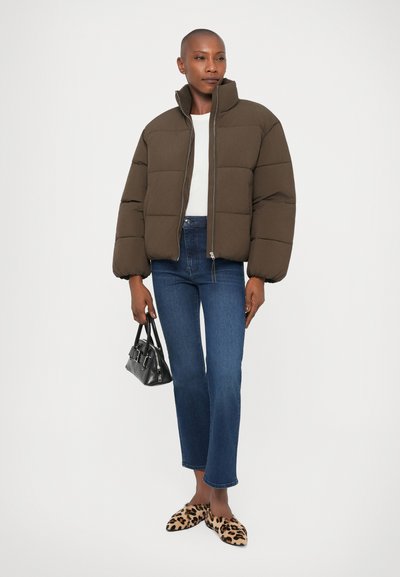 Giacca imbottita marrone con colletto alto, abbinata a jeans blu, slip-on con stampa animale e una piccola borsa nera. Dettagli compatti e testurizzati.