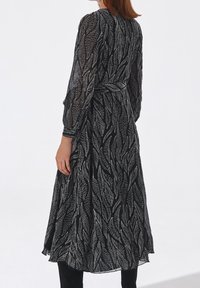 Vestido negro con un patrón de hojas en blanco. Mangas largas, cintura ceñida, falda fluida, hecho de material ligero. Textura translúcida y diseño elegante.