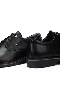Un paio di scarpe eleganti in pelle nera con lacci, tacco basso e un discreto logo del marchio sul lato, presentate su uno sfondo bianco.