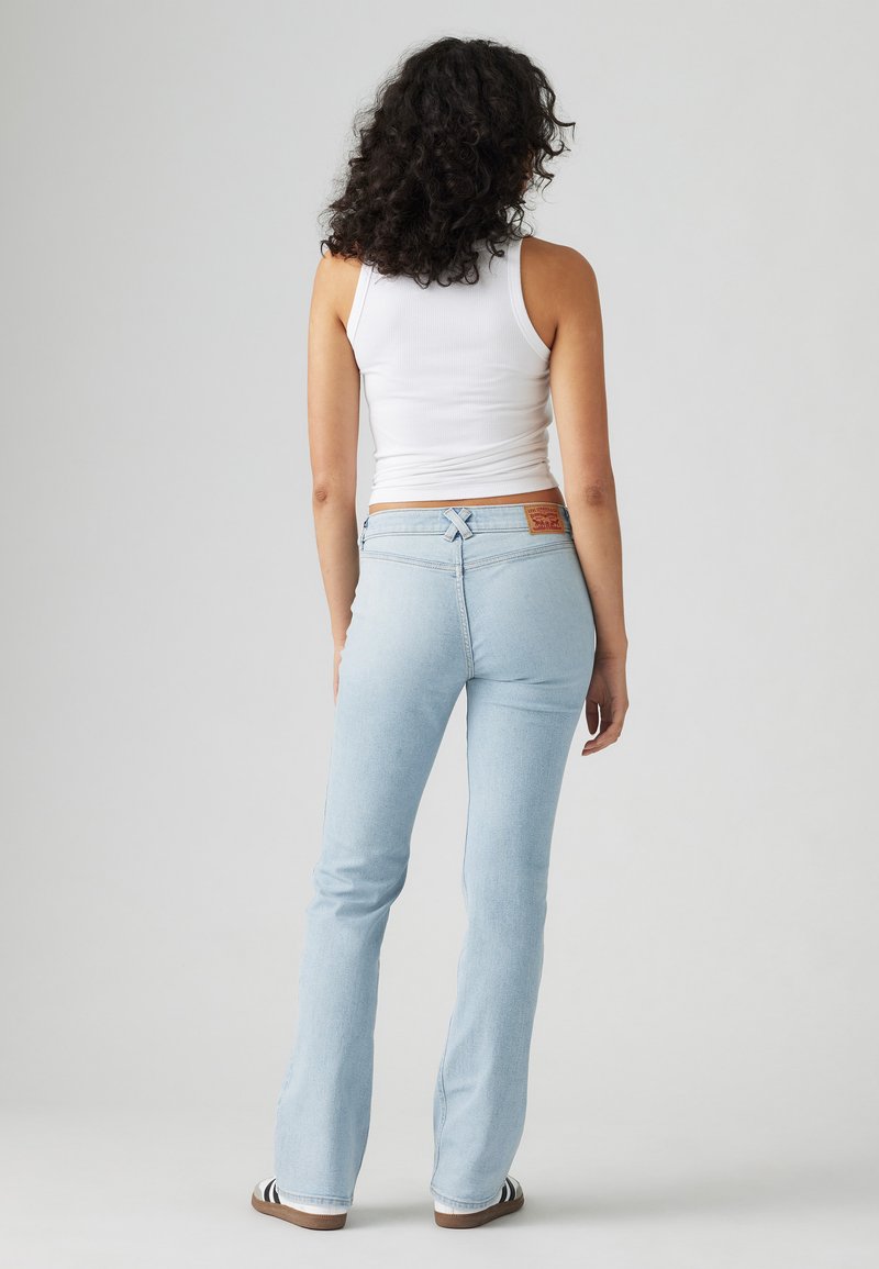 Jean flare bleu clair avec une taille haute, doté d'une ceinture cousue et d'une petite étiquette en cuir à l'arrière pour le détail de la marque.