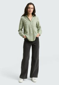 Camicia verde a scacchi con collo e chiusura a bottoni, abbinata a jeans neri a campana e sneakers bianche. Design semplice e informale.