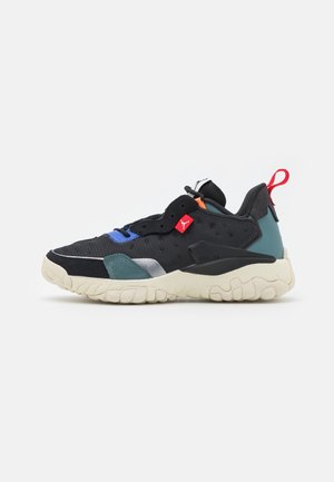 Czarny i wielokolorowy sneaker z kremową podeszwą, czerwoną pętelką do ściągania i małą czerwoną metką z logo z boku, widoczny z zewnętrznej strony.