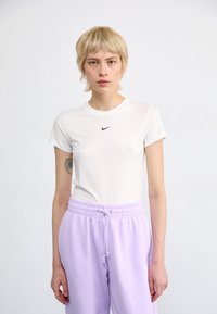 Bílé tričko s krátkým rukávem značky Nike s černým logem, spárované se světle fialovými tepláky s elastickým pasem a bočními kapsami.