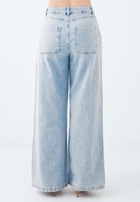 Jeans in denim azzurro chiaro a gamba larga con alta vita, due tasche posteriori, texture sbiadita e orlo rifinito.