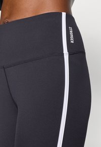 Leggings neri a vita alta con piping bianco lungo il lato, realizzati in tessuto elasticizzato, caratterizzati da una texture liscia e dettagli cuciti.
