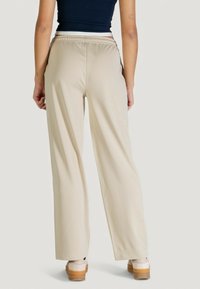 Pantaloni beige a gamba larga con cintura elasticizzata, realizzati in tessuto liscio. La vestibilità è ampia con una silhouette dritta.