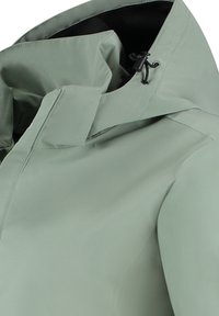 Veste imperméable vert clair avec col haut, cordon de serrage ajustable et texture lisse. Présente une couture minimale et pas de poches externes.