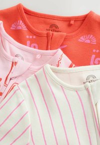 Trois bodies bébé pliés corail avec imprimés soleil, rose clair avec motifs abstraits, et blanc avec rayures roses, montrant les détails de l'encolure.