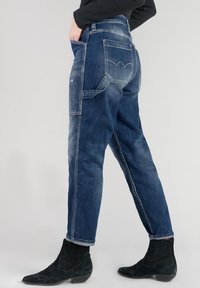 Jeans in denim blu scuro con una vestibilità comoda, caratterizzati da un design a patchwork, molteplici tasche e un particolare dettaglio sulla tasca posteriore.