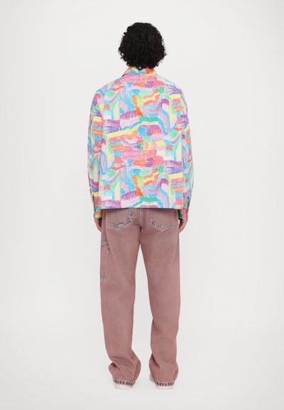 Colorful, patterned jacket with abstract designs in pastels, paired with loose-fitting pink denim pants featuring pockets and a relaxed cut.