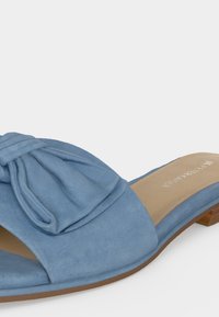 Sandale plate bleu clair à enfiler avec un grand nœud sur la large bride avant et une semelle intérieure beige avec le nom de la marque.