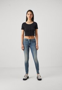 Svart kortärmad t-shirt med knappar, tillsammans med ljusblå åtsittande jeans och blanka silvriga plattformsskor. Släta texturer.
