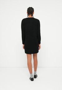 Vestido de suéter de malha preta com mangas compridas, forma ligeiramente justa e tecido texturizado. Apresenta um colarinho redondo e detalhes mínimos.