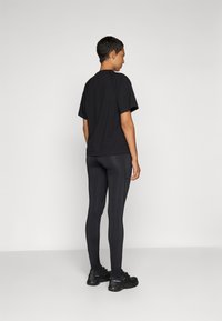 Czarny bawełniany t-shirty z krótkim rękawem zestawiony z czarnymi legginsami. Model nosi czarne buty sportowe. Gładka faktura, prosty design.