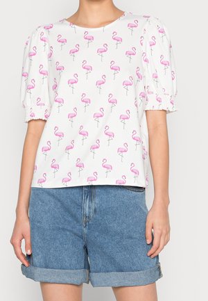 Biały top z krótkim rękawem z bufiastymi rękawkami i różowym nadrukiem flaminga, połączony z podwiniętymi niebieskimi szortami dżinsowymi.