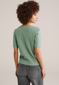 Miętowo-zielony top z krótkim rękawem o fakturowanym trójkątnym wzorze, z prążkowanym dołem i okrągłym dekoltem, w połączeniu z szarymi, wysokim stanem jeansami.