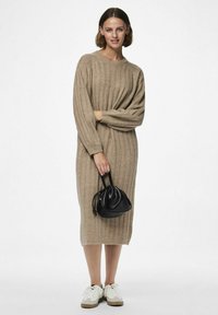Beige ribbat trikåklänning med långa ärmar, mellanhöjd, ihop med en svart handväska och vita sneakers med ljusgrå detaljer.