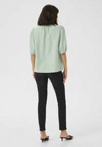 Blouse texturée vert menthe avec des manches courtes bouffantes, associée à un jean slim noir et des mules noires à talons avec un accent nœud.