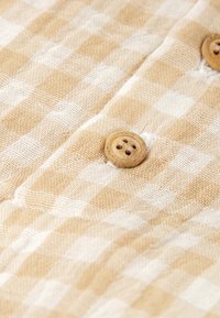 Tela a cuadros en tonos beige y blanco con una superficie texturizada, adornada con botones de madera. El patrón consiste en cuadros alternos.