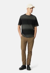 Zwart-grijs gestreept shirt met korte mouwen, kaki broek, zwarte schoenen en een beige pet. Eenvoudig ontwerp met een ontspannen pasvorm en een gladde textuur.