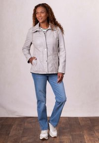 Light gray leather jacket with a button-up front, elastic drawstrings, and two side pockets, paired with blue jeans and white sneakers.