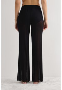 Zwarte, geribbelde, wijde broek met hoge taille en zijsplitsingen, gemaakt van een lichtgewicht, halftransparante stof. Geen zichtbare hardware of accenten.