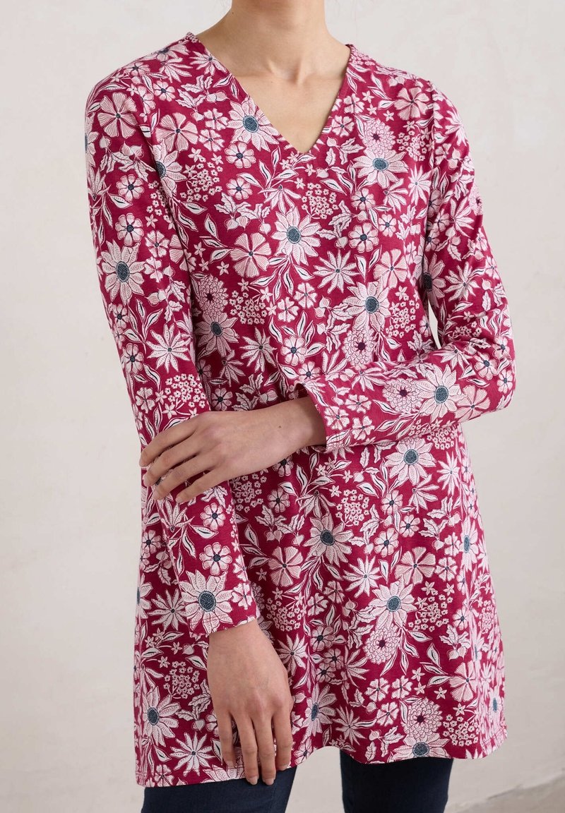 Czerwona tunika w kwiaty z dekoltem w serek, długimi rękawami i skomplikowanymi białymi oraz niebieskimi wzorami kwiatowymi. Miękka, teksturowana tkanina.
