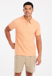 Korte mouw polo in pasteloranje katoen met een klassieke kraag, twee knopen sluiting en ribgebreide manchetten, gecombineerd met beige shorts.