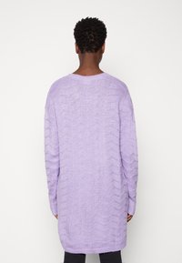Lila übergroßer Strickpullover mit einem strukturierten Zickzackmuster, langen Ärmeln und einem runden Halsausschnitt, der über die Hüften reicht.