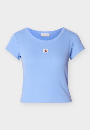 Világoskék bordázott pamut rövid ujjú póló, amelyen egy kis téglalap alakú logófolt található a mellkasnál, valamint lekerekített nyakkivágás.