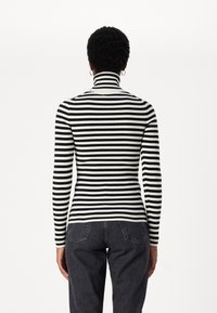 Maglione a collo alto a righe bianche e nere con texture a coste, maniche lunghe e silhouette aderente, abbinato a jeans scuri.
