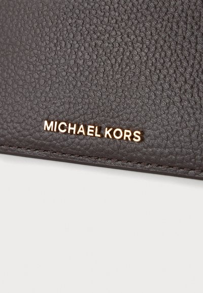 Surface en cuir texturé marron avec des lettres métalliques dorées formant le nom Michael Kors près du bord cousu.