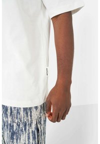 Witte korte mouwen t-shirt met een zijlabel, gecombineerd met blauw-witte geblokte broek. De stof lijkt zacht en heeft een relaxte pasvorm.