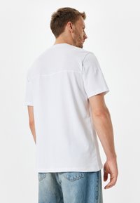 Witte t-shirt met korte mouwen en een ronde hals, gemaakt van gladde katoen, met een naaddetail aan de achterkant en een relaxte pasvorm. Gecombineerd met lichtblauwe jeans.
