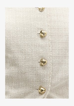 Tissu en crêpe tissé crème avec rangée verticale de quatre boutons en métal doré torsadés, bords texturés le long de la couture des boutons.